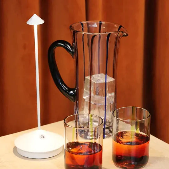 Karaffe mit Eiswürfeln, zwei Gläser mit Getränk, weiße Tischlampe, modernes Design.